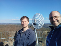 Tim und Wolfgang stehen auf dem Rehbergturm vor einem WLAN-Spiegel
